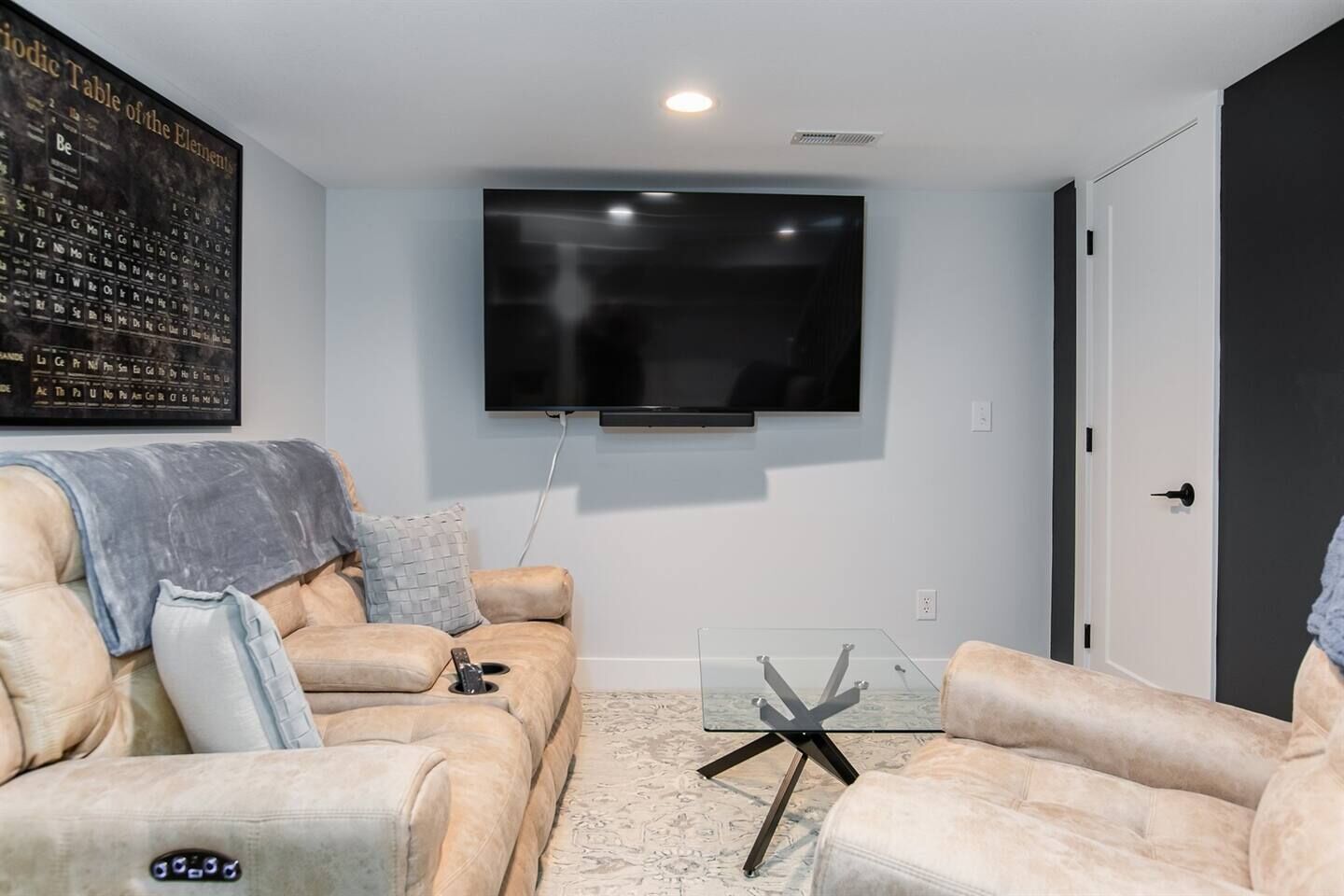 A living room with a flat-screen TV mounted on the wall, a sofa, and two armchairs.