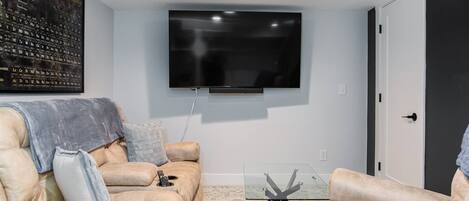 A living room with a flat-screen TV mounted on the wall, a sofa, and two armchairs.