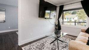 A modern living room with a flat-screen TV mounted on the wall, a glass coffee table, a beige sofa, and a patterned rug. - Modern 3 bed 4 bath home just 5 mins to ND (1446) (South Bend)