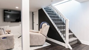A modern living room with a flat-screen TV, a beige sofa, and a staircase with a black railing. - Modern 3 bed 4 bath home just 5 mins to ND (1446) (South Bend)