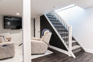 Un salon moderne doté d’un téléviseur à écran plat, d’un canapé beige et d’un escalier avec une rampe noire.