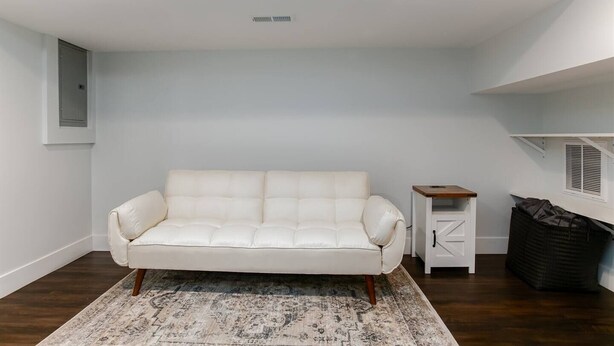 A white leather sofa in a room with a patterned rug, a small wooden side table, a white cabinet, and a black wicker basket. - Modern 3 bed 4 bath home just 5 mins to ND (1446) (South Bend)