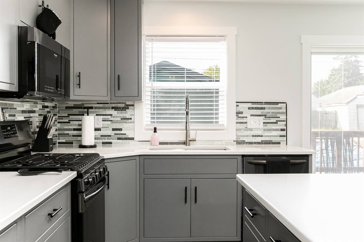 A modern kitchen with grey cabinets, a stainless steel range, and a window with blinds.