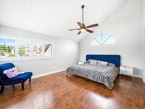 A bedroom with a bed, a ceiling fan, a window with blinds, and a view of buildings outside. - Charming 3-bedroom house with AC in peaceful Moreno Valley (Moreno Valley)