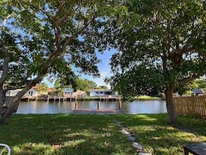 A lakeside property with a dock, grassy areas, and a pathway leading to a wooden deck.