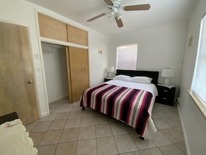 A bedroom with a bed, a wardrobe, a ceiling fan, and a window with blinds.