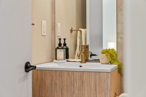 A bathroom with a wooden vanity, a gold faucet, and two black bottles on the counter. - The Edison Old City | Premier 1 BR Suite w/ City View + Shared Roofdeck (Philadelphia)
