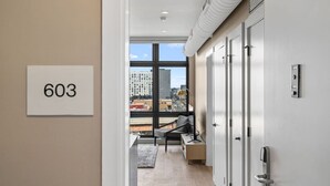 A modern hotel room with a large window, a sofa, a desk, and a view of the cityscape. - The Edison Old City | Premier 1 BR Suite w/ City View + Shared Roofdeck (Philadelphia)