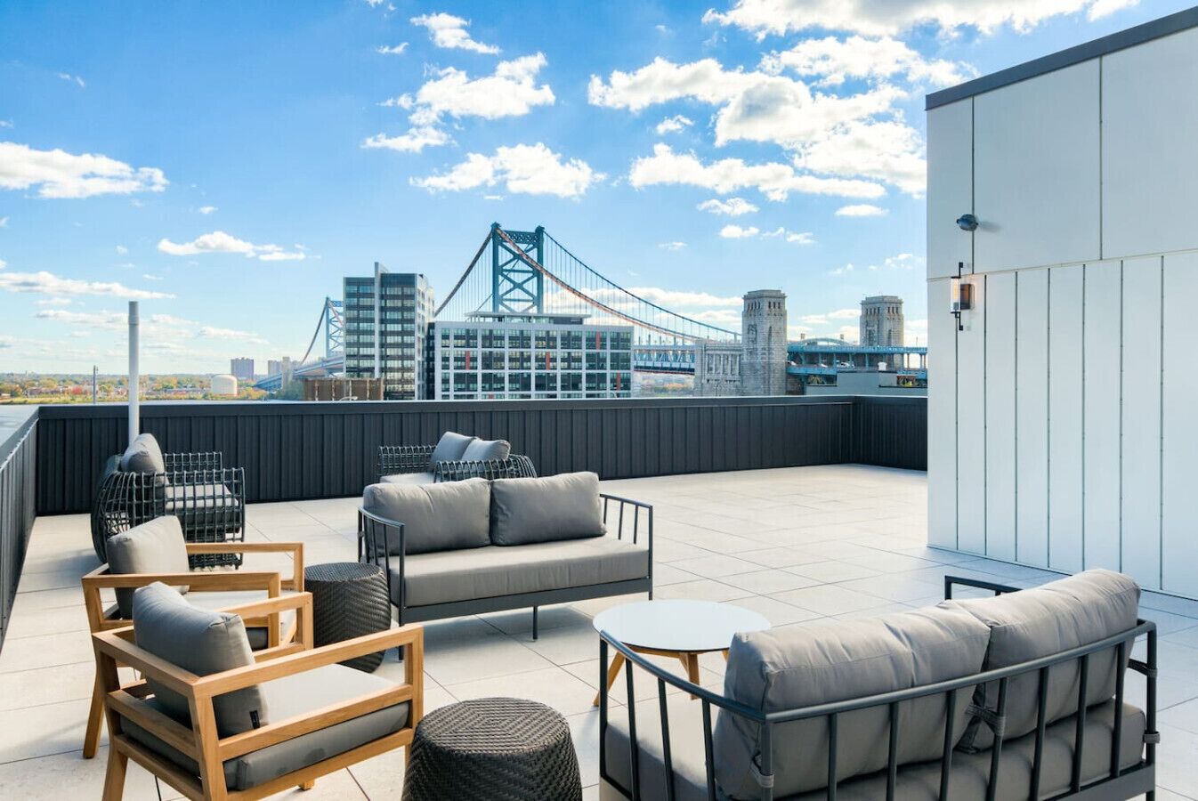 A rooftop terrace with outdoor seating, a view of a bridge, and modern buildings in the background.