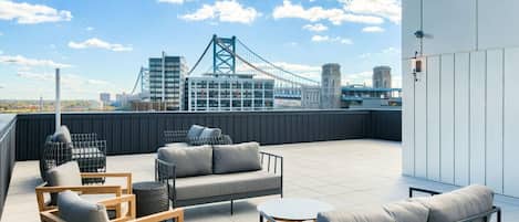 A rooftop terrace with outdoor seating, a view of a bridge, and modern buildings in the background.
