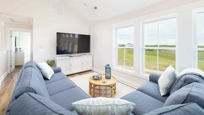 A modern living room with a large sofa, a television, and a view of the outdoors. - New Corolla Home with Pool & Spa! (Corolla)