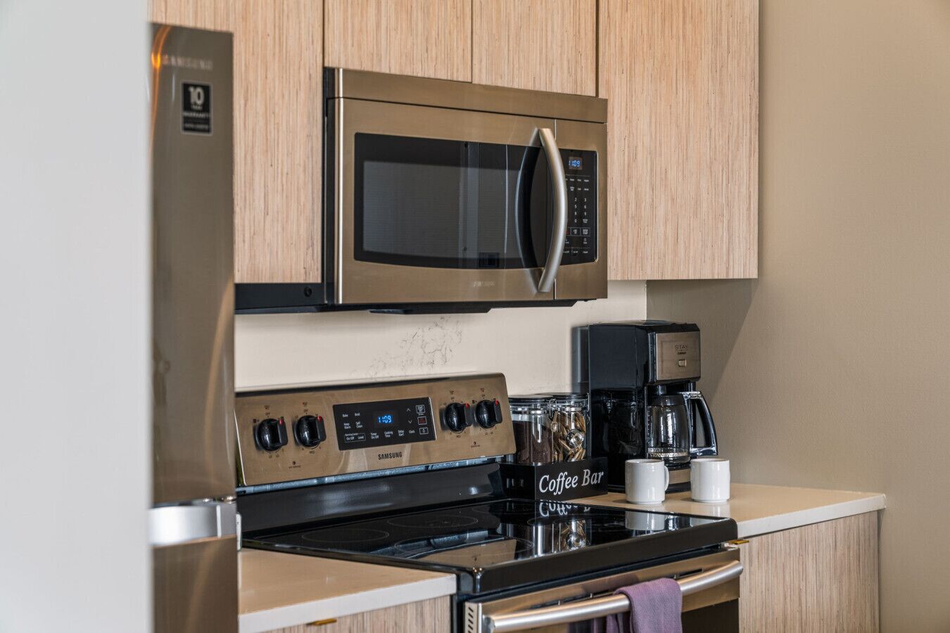 A kitchen with a stainless steel microwave, a coffee maker, and a Samsung stove.