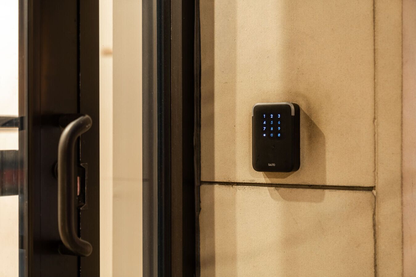 A keypad lock on a beige wall, a door handle, and a glass door.