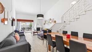 Un salon moderne comprenant un canapé, une table à manger et des chaises, un escalier et un balcon avec un espace salon extérieur.