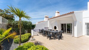 Une terrasse avec des meubles d’extérieur, un mur en briques et un bâtiment blanc avec un toit recouvert de tuiles.