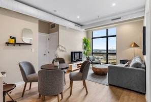 A modern living room with a sofa, chairs, a coffee table, a TV, and a large window with a view. - The Edison Old City | Premier 2 BR Suite w/ River View + Shared Roofdeck (Philadelphia)