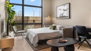 Een moderne hotelkamer met een groot raam, een bed, een bureau, een stoel en een tafeltje.