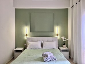 Un lit bien fait, avec des oreillers et une serviette enroulée, deux tables de chevet et un luminaire fixé au mur.
