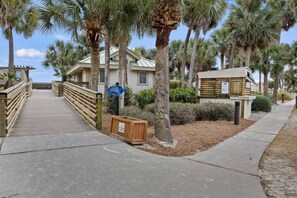 A wooden boardwalk leading to a beachfront property with palm trees and a clear sky. - Golf Course Corner Villa First Floor Views (Hilton Head Island)