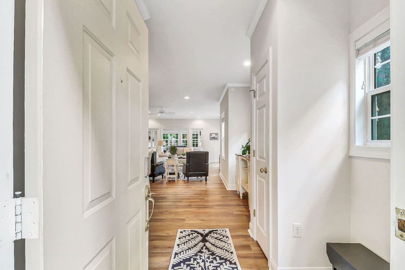 A hallway with a patterned rug, wooden flooring, and a view into a living area with furniture.