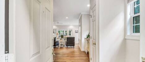 A hallway with a patterned rug, wooden flooring, and a view into a living area with furniture.