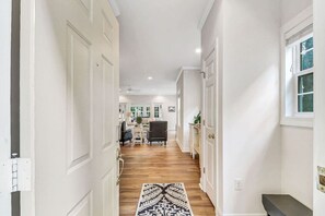 A hallway with a patterned rug, wooden flooring, and a view into a living area with furniture. - Golf Course Corner Villa First Floor Views (Hilton Head Island)