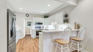 A modern kitchen with white cabinetry, a central island with bar stools, a refrigerator, and a microwave. - Golf Course Corner Villa First Floor Views (Hilton Head Island)