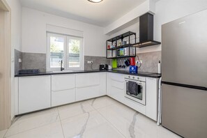 Una cocina moderna con armarios blancos, horno empotrado, refrigerador de acero inoxidable y una ventana que proporciona luz natural.