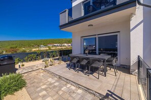 Un patio exterior moderno con una mesa y sillas, una parrilla y vistas a un paisaje verde.