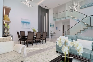A modern living room with a dining area, a staircase, and a sofa with white flowers.