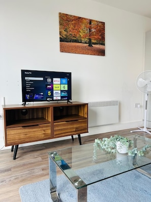 Ein modernes Wohnzimmer mit Flachbildfernseher, einer Holz-Unterhaltungseinheit, einem Glastisch und einem Bild an der Wand.