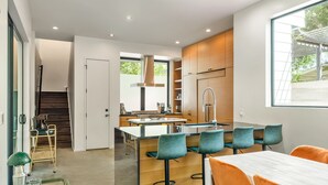 Een moderne keuken met een centraal eiland, barkrukken en een eettafel met stoelen.