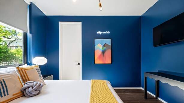 A bedroom with a bed, a bedside table, a TV mounted on the wall, and a door. - Rainey Retreat / Pool / Hot tub / Firepit / DT ATX (Austin)