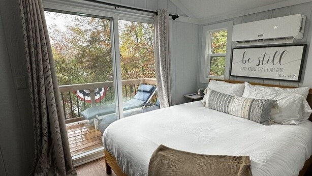 A bedroom with a large bed, a view of the outdoors, a ceiling fan, and a motivational quote on the wall. - Tremendous 4-bedroom house with Boat Dock, Pool and Hot Tub in charming Harriman (Harriman)