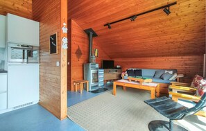 Interior de una cabaña de madera con kitchenette, un sofá, una mesa de centro y una chimenea.