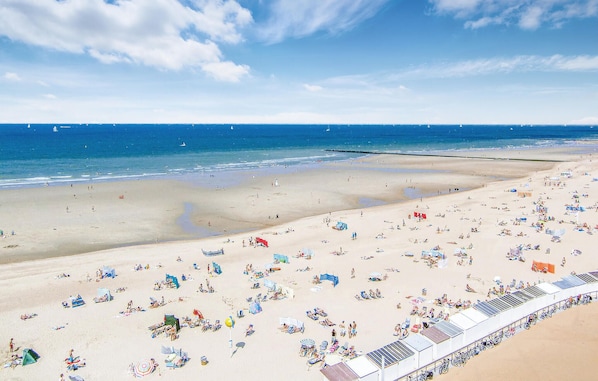 A beach with numerous sunbeds and umbrellas, a sandy shore, and a clear blue sky.
