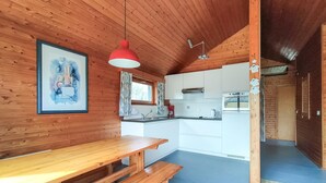 A wooden interior with a dining table, a red pendant light, a kitchen with white cabinets, and a framed painting on the wall. - 2 bedroom nice home in Westende (Westende)