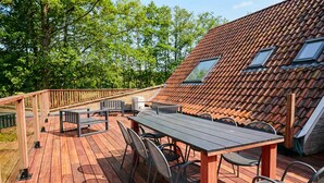 A wooden deck with a table and chairs, a railing, and a house with a tiled roof and skylights. - Gorgeous home in Knesselare with sauna (Knesselare)