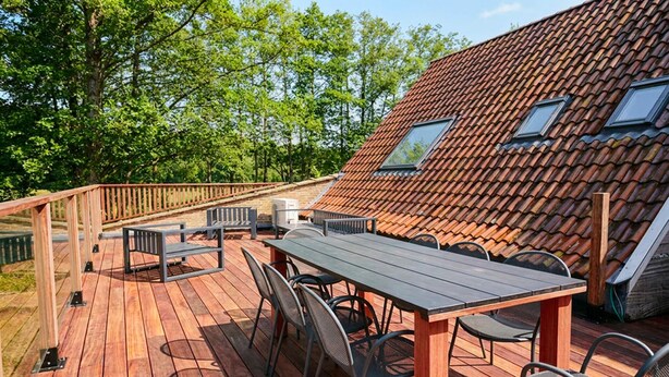 A wooden deck with a table and chairs, a railing, and a house with a tiled roof and skylights.