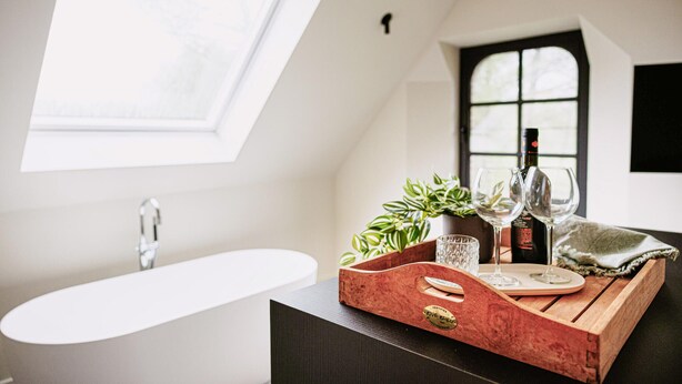 A modern bathroom with a freestanding bathtub, a window, and a wooden tray with wine glasses and a bottle. - Gorgeous home in Knesselare with sauna (Knesselare)