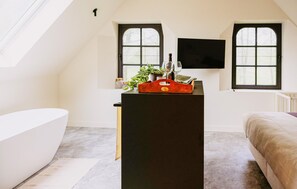 A room with a black desk, two windows, a white bathtub, and a bed.