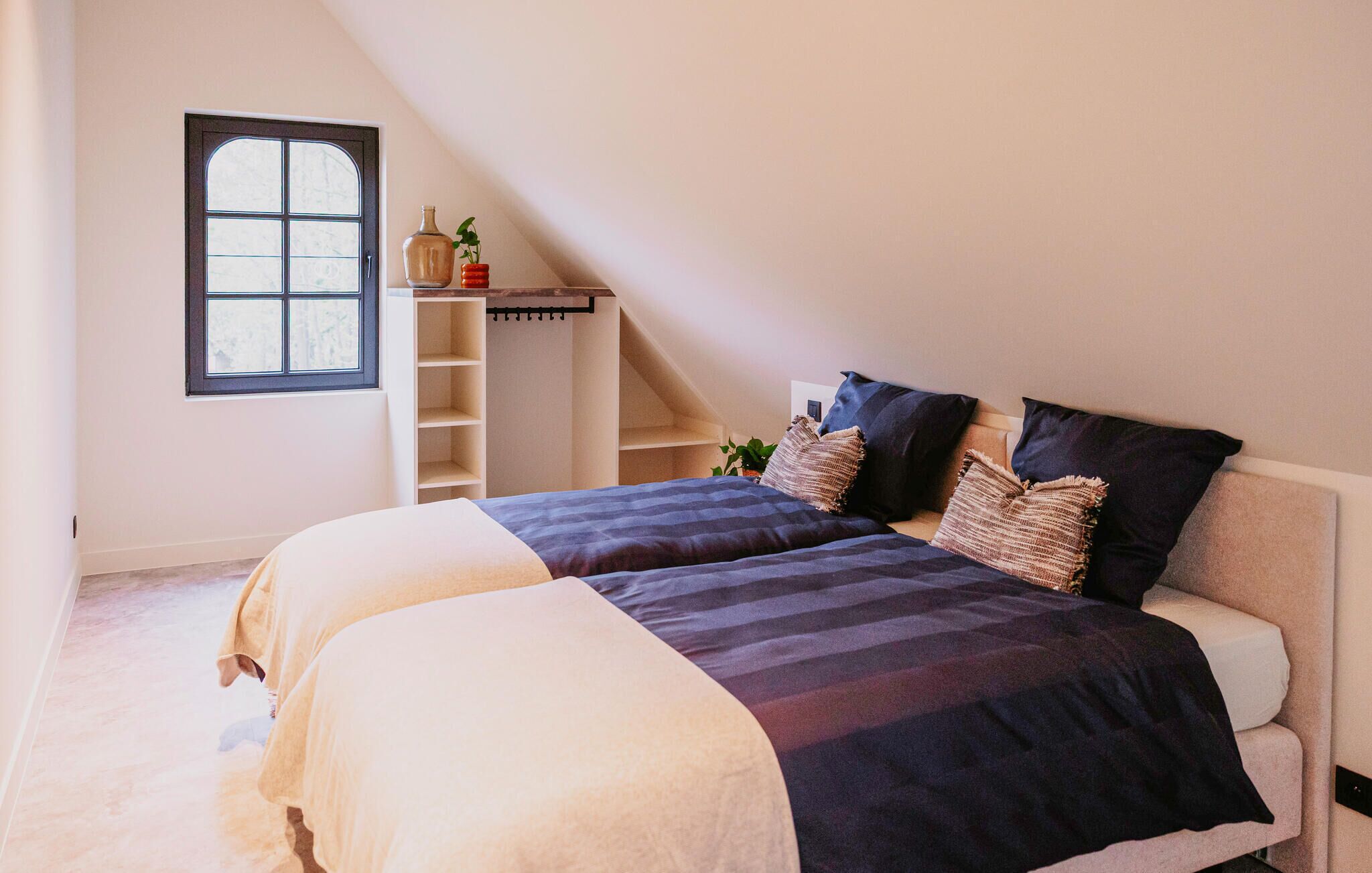 A bedroom with a bed, a window, a shelf with decorative items, and a staircase.