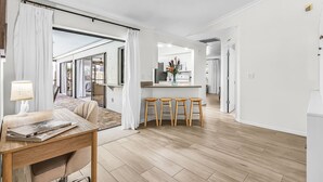 Ein modernes Interieur mit einem Holztisch, Barhocker, einer Küchenzeile und einem Wohnbereich mit einer Couch und Vorhängen.