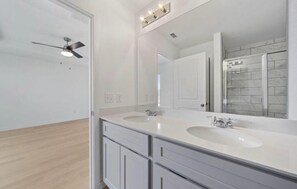 A modern bathroom with two sinks, a large mirror, and a ceiling fan. - Charming 4-bedroom house in enjoyable Buda in sunfield community with Lazy River (Buda)