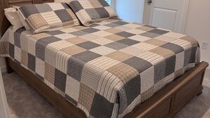 Ein Schlafzimmer mit einem hölzernen Kopfende, einer karierten Bettdecke und einem Teppichboden.