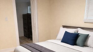 Een slaapkamer met een bed, een houten hoofdbord, een donge dekbedovertrek en een raam met jaloezieën.