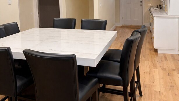 Een eetruimte met een marmeren tafel en zwarte stoelen, een keuken met witte kasten en een houten vloer.