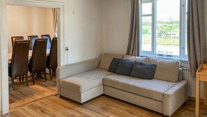 A living room with a beige sectional sofa, a dining table with chairs, and a window with curtains. - Stunning home in Lemvig with WiFi (Lemvig)