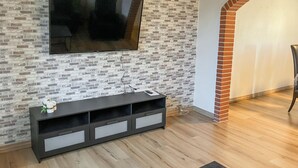 A living room with a brick-patterned wall, a flat-screen TV mounted above a dark wooden entertainment unit, and a wooden floor. - Stunning home in Lemvig with WiFi (Lemvig)