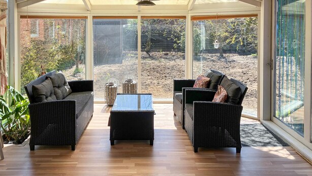 A sunroom with wicker furniture, large windows, and a view of a garden. - Stunning home in Lemvig with WiFi (Lemvig)